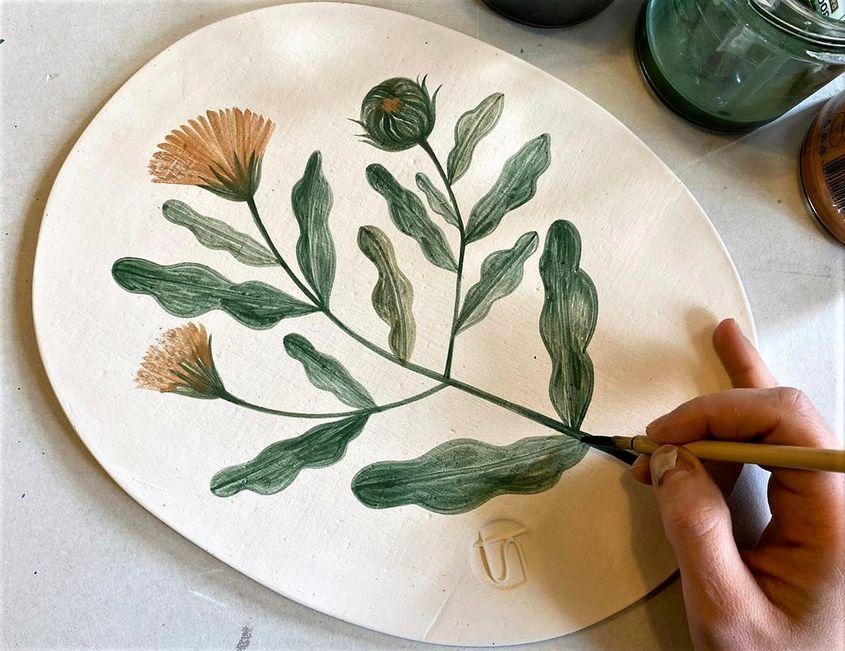 Irina Silivestru pictează o plantă pe un platou de ceramică