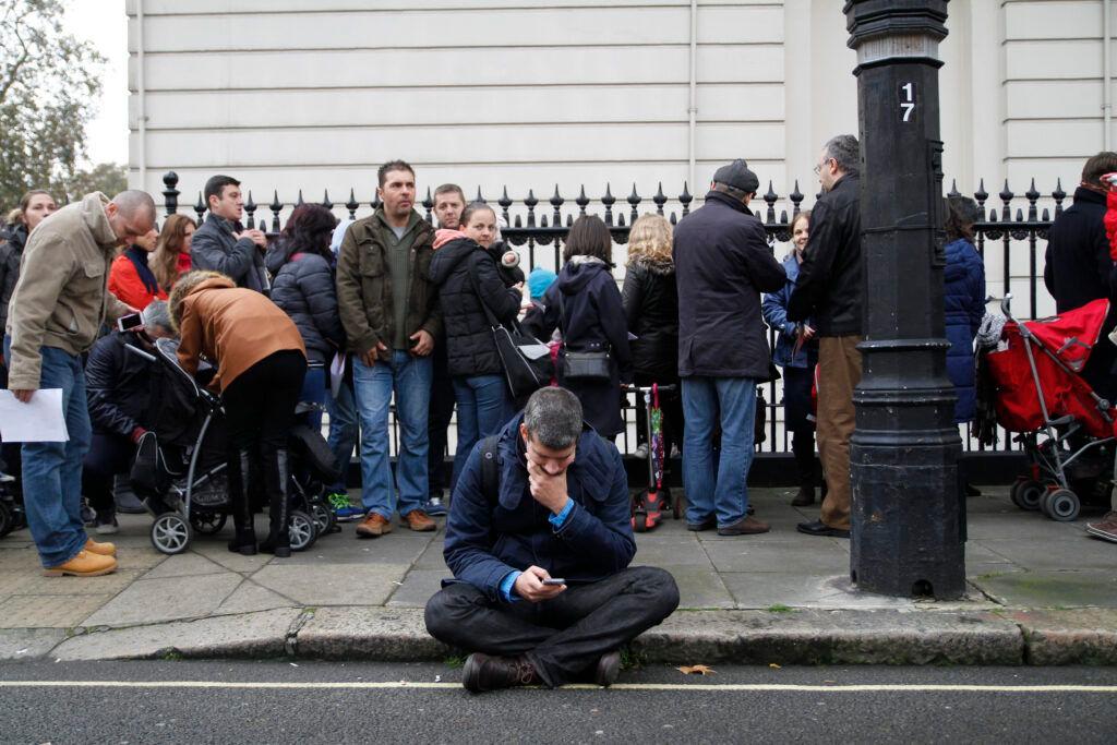 Un bărbat își privește telefonul așezat pe o bordură, langă coada formată de cetățenii români veniți să voteze la o secție din Londra, duminică, 16 noiembrie 2016. Foto: Inquam Photos/Adriana Neagoe