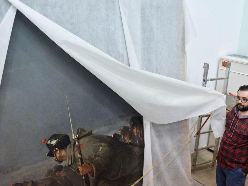 Un angajat al Muzeului Național de Istorie a României dezvelește pictura "Atacul de la Smârdan", de Nicolae Grigorescu, depozitată în spatele unui perete de expoziție. Foto: Lucian Muntean