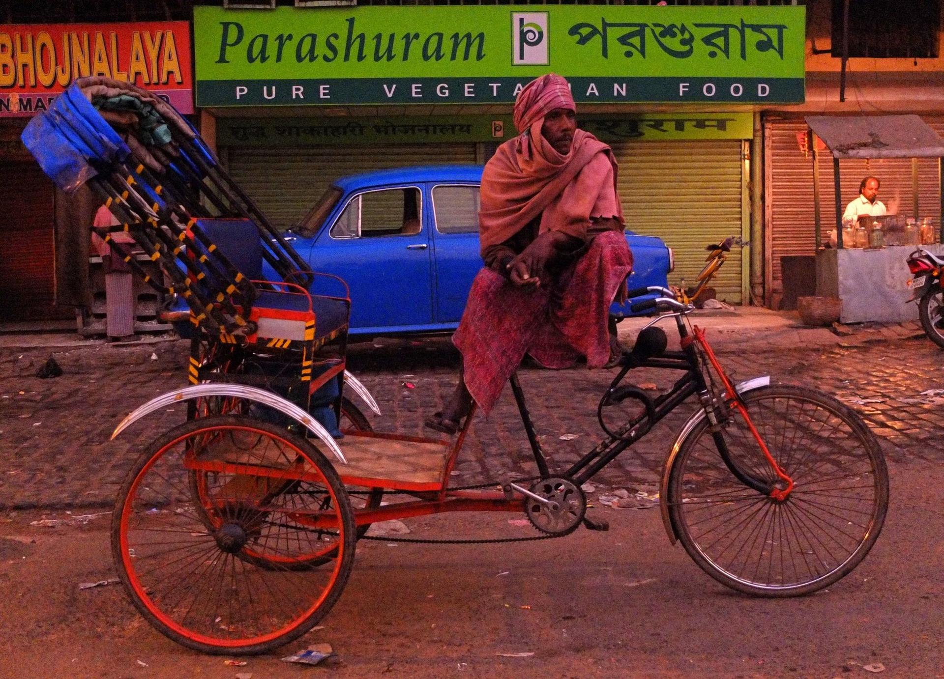 Seara târziu, un ricșar biciclist mai speră să agațe niște ultimi clienți într-un cartier sărac.