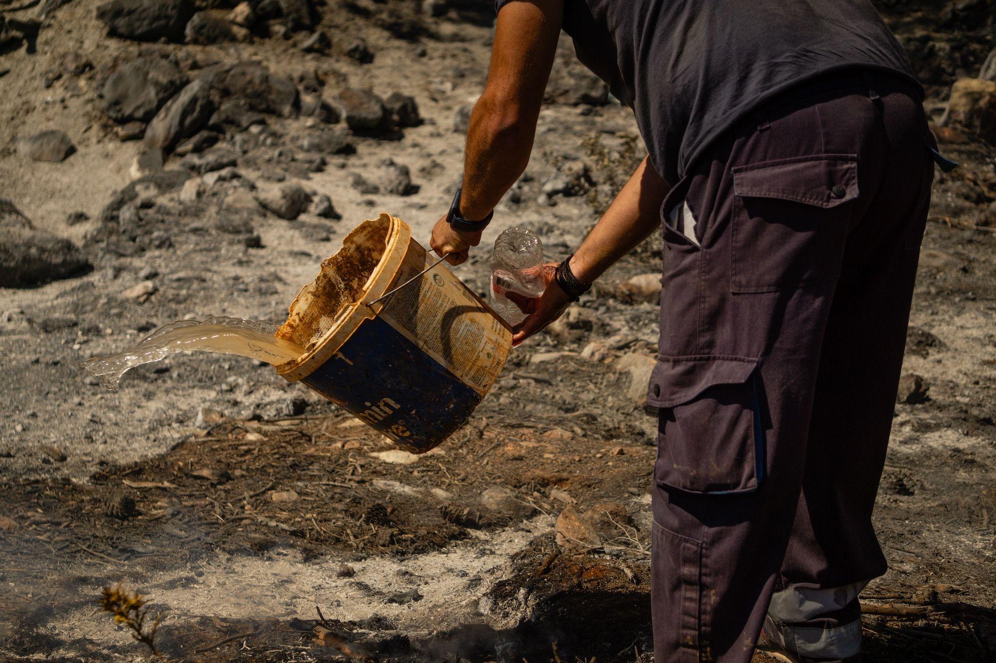 A municipal worker in Nea Makri continues to douse the ground with water, fighting to extinguish the remaining hot spots left by the destructive wildfires that have swept through East Attica since Sunday. Photo: Ioana Epure