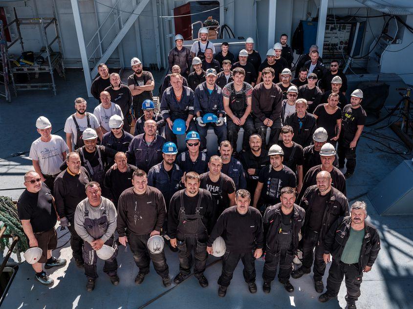 „O parte din echipa de 80 de electricieni navali români. Cei care lipsesc din imagine erau în concediu în România sau lucrau pe vapoare în altă parte a portului. Șantierul naval Karstensens, Skagen, Danemarca” <strong>Foto ©: Cosmin Bumbuț, Teleleu</strong>