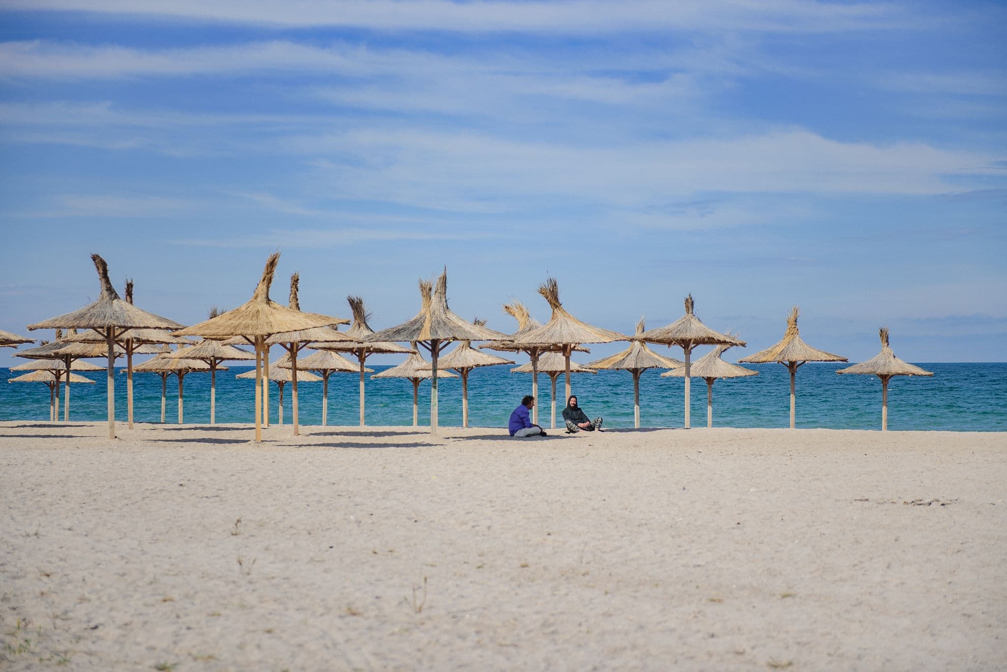 În Vama Veche, doi oameni stau de vorbă direct pe nisip sub umbrelele de stuf care, în mai puțin de două zile, vor adăposti șezlonguri așezate regulamentar la distanță de 2 metri unele de altele.