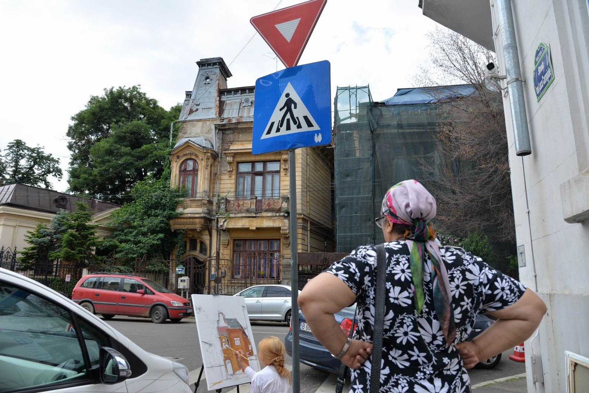 O femeie o privește pe Maria Jardă cum pictează între mașini pe strada Ion Luca Caragiale din București. Foto Lucian Muntean