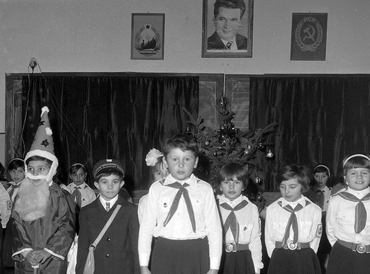 <em>Grup de pionieri cu ocazia Sărbătorilor de iarnă, cu un pom stingher </em>în fundal <em>și un Moș Gerilă de inspirație sovietică, cu barbă. Cuvântul Crăciun a fost eliminat</em> din vocabular.