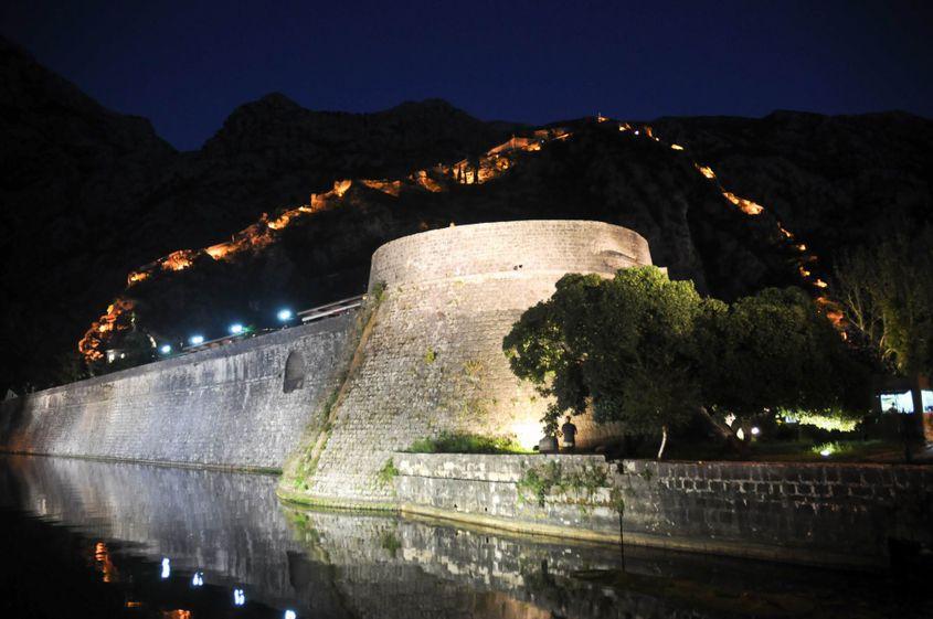 Zidul masiv din prim-plan străjuiește centrul istoric. În fundal se distinge fortificația medievală de pe versantul muntelui.