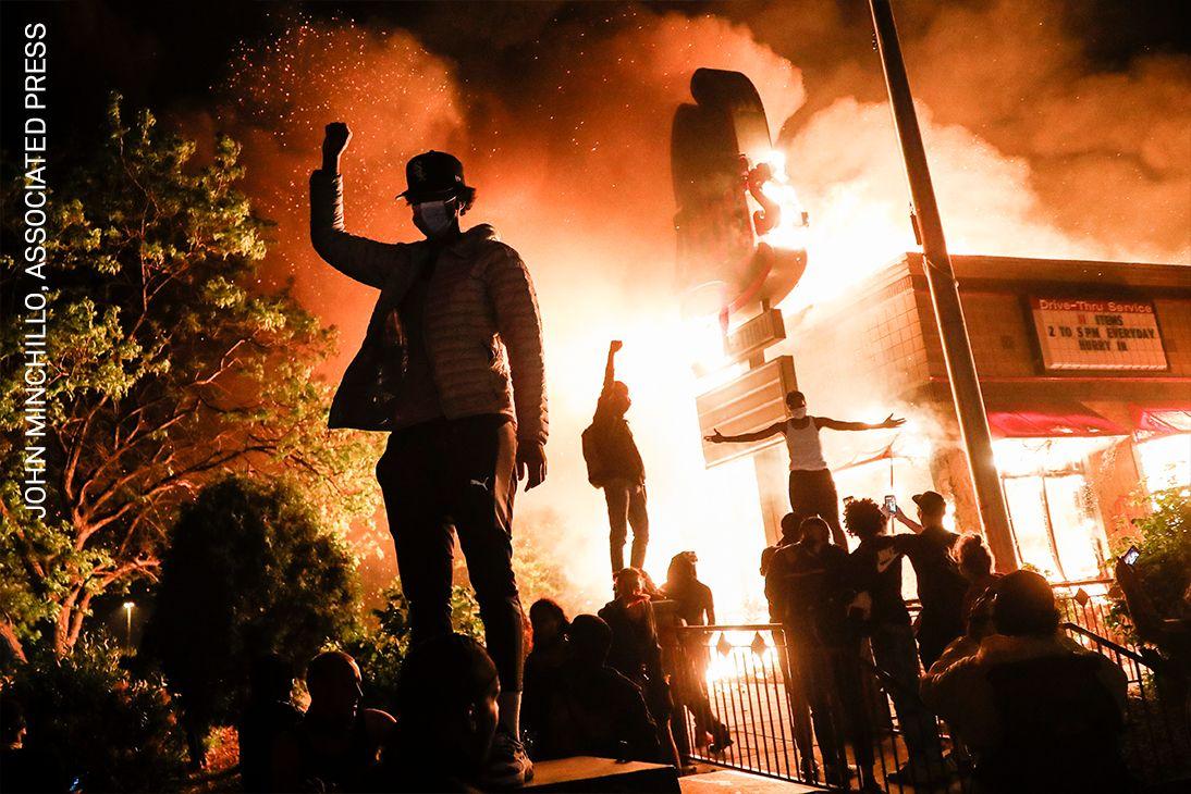 Protestatarii își ridică pumnii drept sfidare în fața unui restaurant fast-food incendiat, lângă secția de poliție a ofițerilor care l-au arestat pe George Floyd, în Minneapolis, SUA.