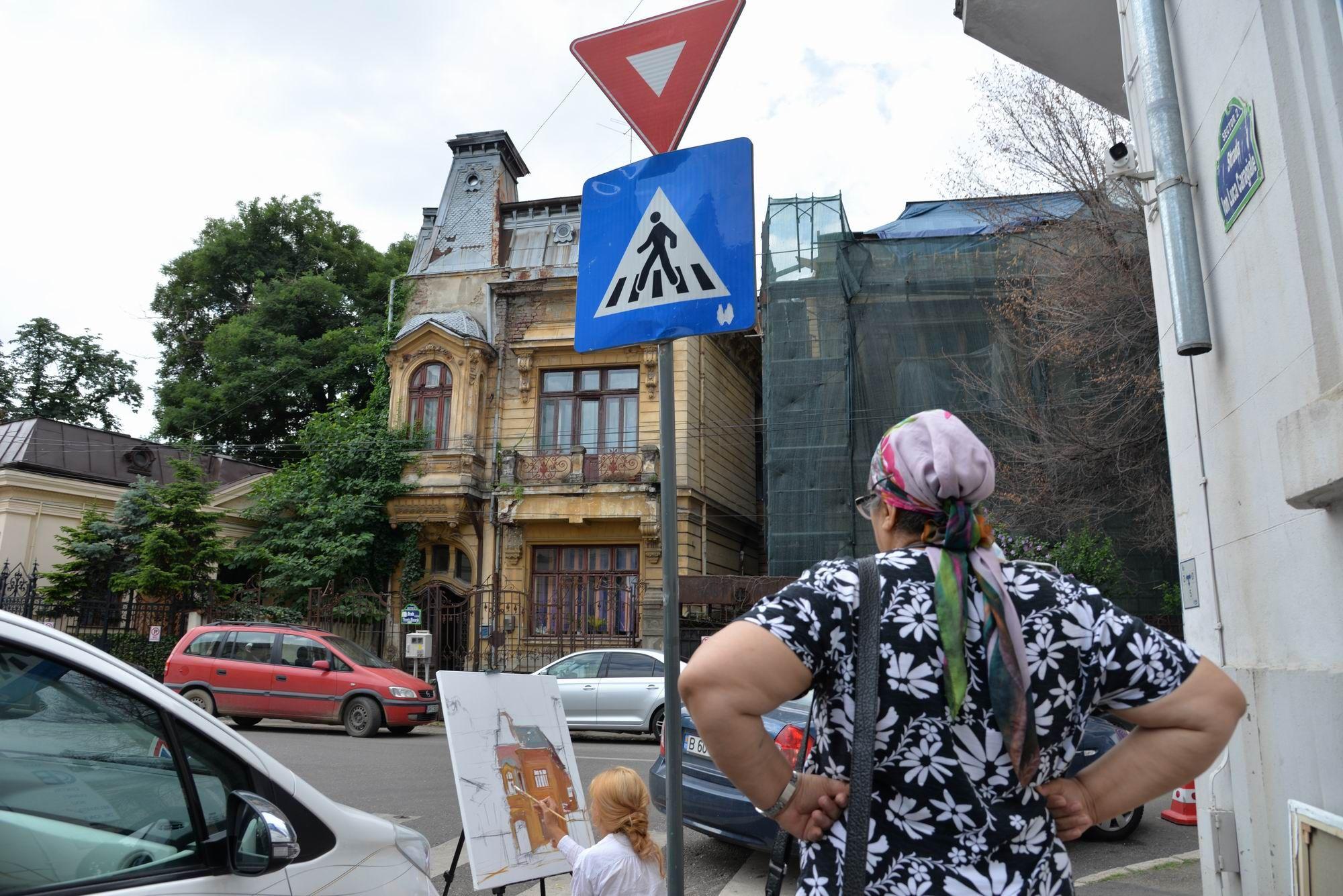 O femeie o privește pe Maria Jardă cum pictează între mașini pe strada Ion Luca Caragiale din București. Foto Lucian Muntean