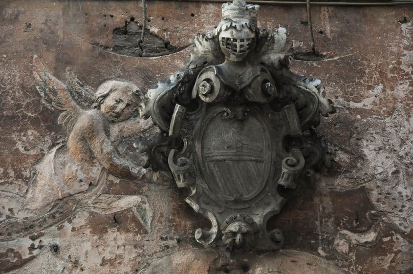 Un basorelief în stil baroc flanchează blazonul de pe fațada unei vechi case din Kotor.