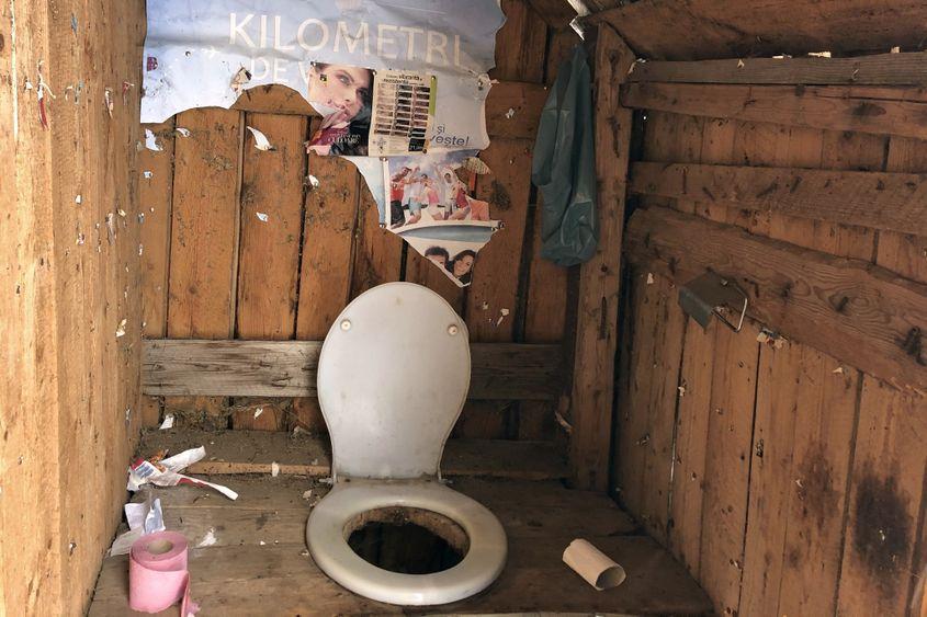 Interior de toaletă din vecini, cu colac modern și cândva tapetat cu afișe.