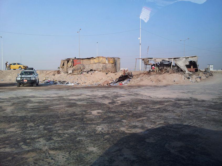 Irak, Basra. „După ieșirea din aeroport, erai așteptat de cei de la firma de securitate care te transportau in câmpul unde urma sa muncești. Acele copertine improvizate erau și spațiu comercial și loc de așteptare”. Foto: Alex Ciupitu