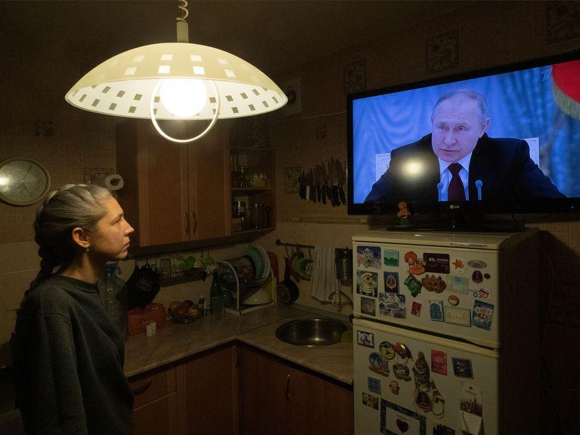 O femeie privește în timp ce președintele rus Vladimir Putin ține un discurs pe tema Ucrainei. Foto: EPA/Anatoly Maltsev