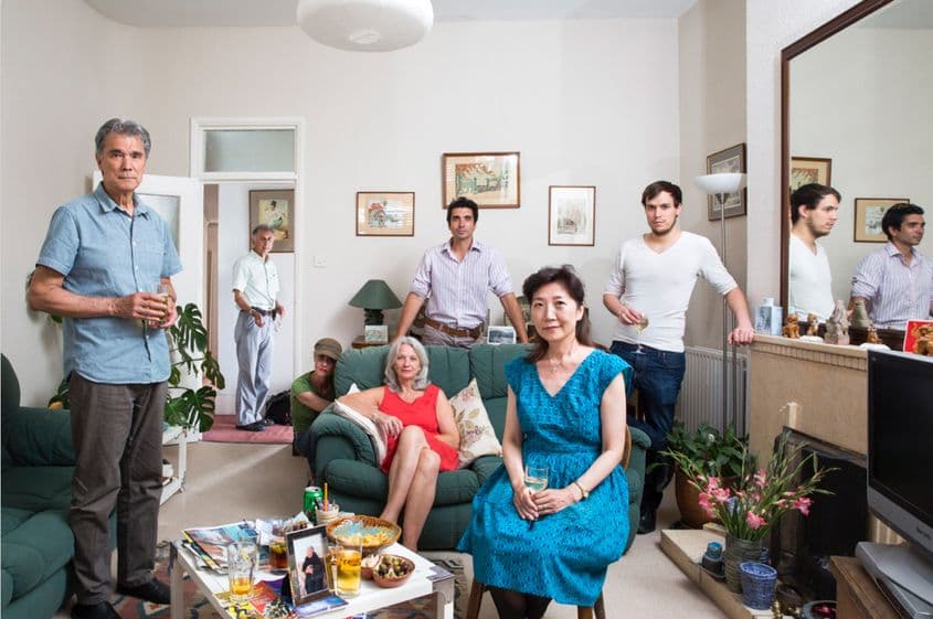 Familie din Myanmar, Anglia, Australia & Japonia: fotograful Chris Steele-Perkins (în plan îndepărtat, în cadrul ușii), soția sa − Miyako Yamada (în albastru) și fiul lor Cedric (lângă oglindă). Fratele vitreg al lui Chris este Thein Mynt (în stânga, cu paharul în mână), soția sa − Jean Miller (în roșu), fiul lor − Lewin (în mijloc) și partenera acestuia − Francis (în verde, lângă canapea). „Aici, oamenii mă întreabă de multe ori de unde sunt, din cauza accentului. Dar mulți nu știu de Burma. Întreabă: Bermuda?”, spune Thein Mynt, care s-a născut în Burma. „Unii britanici au membri ai familiei care au luptat în război acolo, dar ei nu știu asta”. Foto: Chris Steele-Perkins